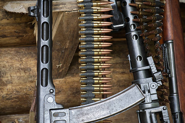 istock Close-Up of Machine Gun with Ammunition and Rifles Displayed in Rustic Setting 2216180985
