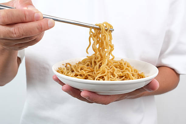 Hand holding chopsticks to eat spicy instant noodles on plate