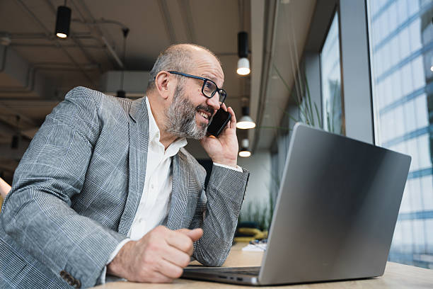 istock Smiling Businessman Speaking on Smartphone While Working on Laptop in Office 2216187152