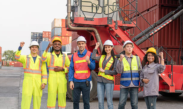 istock Diverse Team of Industrial Workers Celebrating at Shipping Container Yard, Multiracial Logistics Crew in Safety Gear Posing with Team Spirit 2216190766