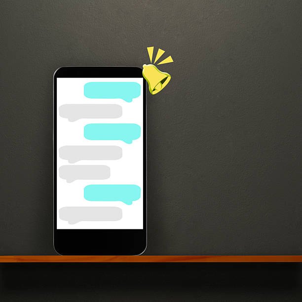 Smartphone with notification bell icon for online chat bubble on a wooden shelf against dark concrete wall.