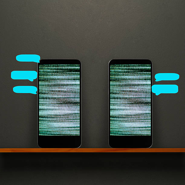 Close-up of two grainy screen smart phone with blue speech bubbles on a wooden shelf against dark concrete wall.