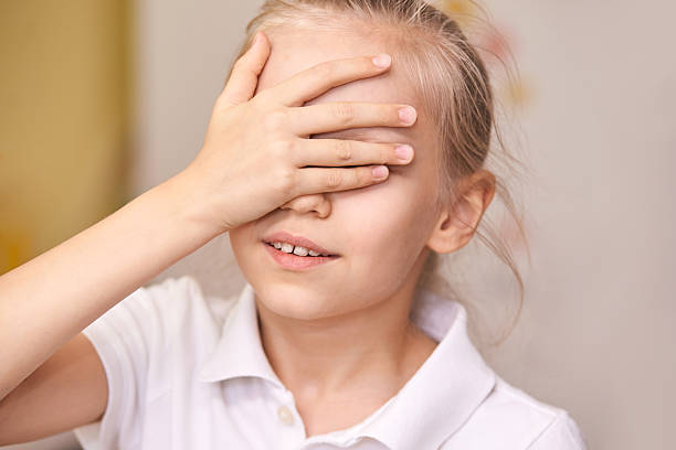 Young caucasian girl covering eyes with hand wearing white polo shirt indoors Young caucasian girl covering eyes with hand wearing white polo shirt indoors. hair covering eyes stock pictures, royalty-free photos & images