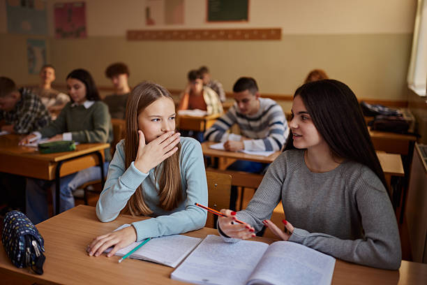 istock Smiling female students whispering on a class at high school. 2216199305