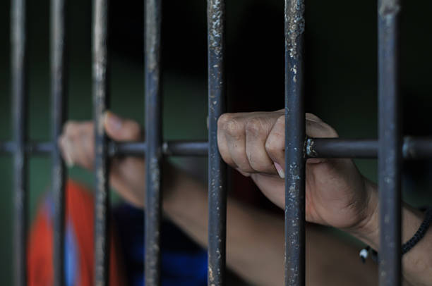istock hands of a prisoner behind prison bars on black background 2216200104