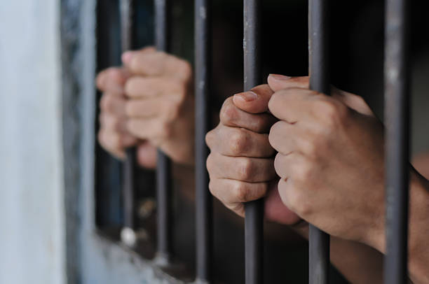 istock hands of a prisoner behind prison bars on black background 2216200164
