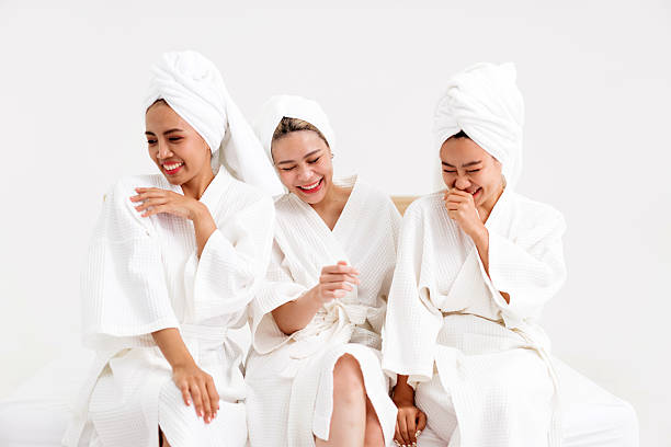 Three women in white bathrobes and towels laugh together during a spa day, capturing friendship, relaxation, and joy. Perfect for wellness, beauty, and lifestyle content with spa-related themes.