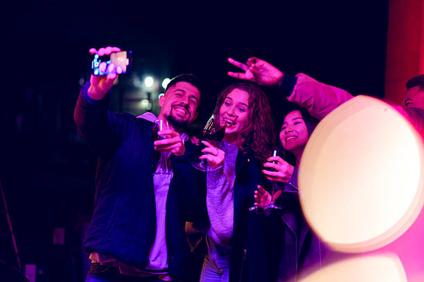 istock Group of friends celebrating at night with drinks and laughter while taking selfies at a lively party 2216205610