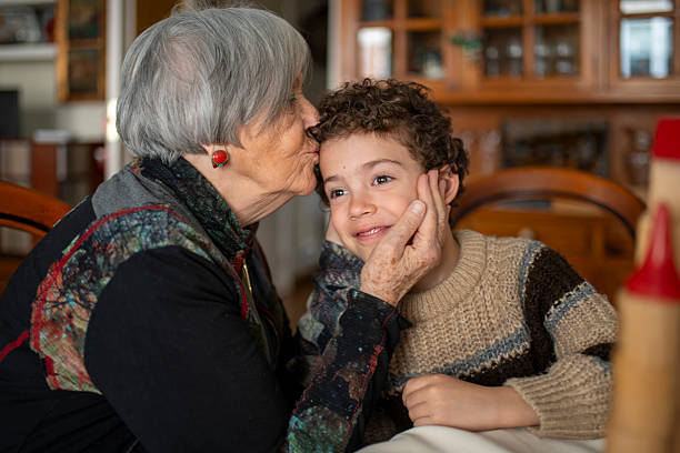 Grandmother is giving a kiss on the forehead of her grandson while caressing his face, showing affection and tenderness