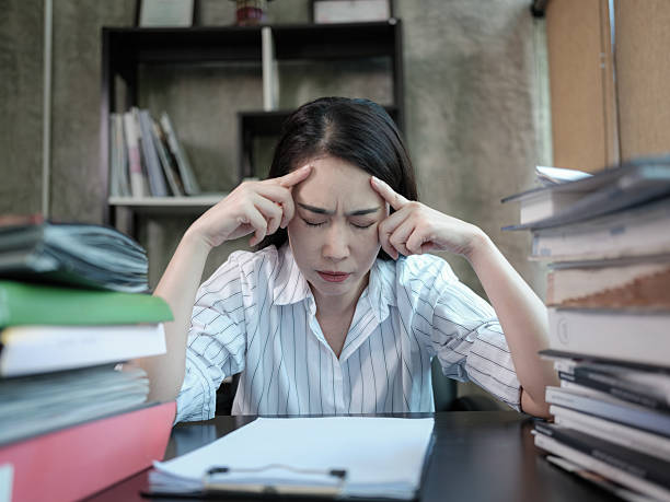 istock Asian businesswoman concentrating while working on a stack of paperwork on her desk. 2216208755