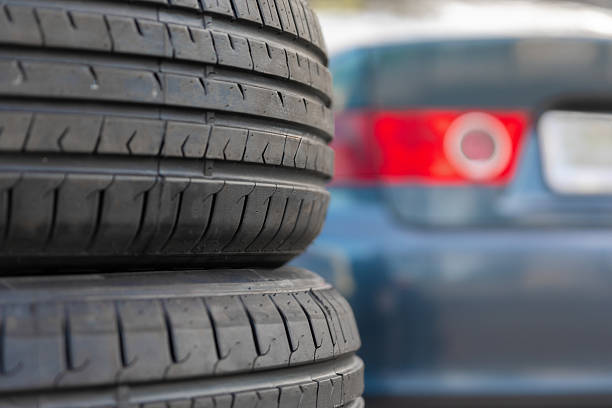 Horizontal stack of used tires with visible tread, positioned in front of a blurred blue car, suitable for auto service or transportation concepts.