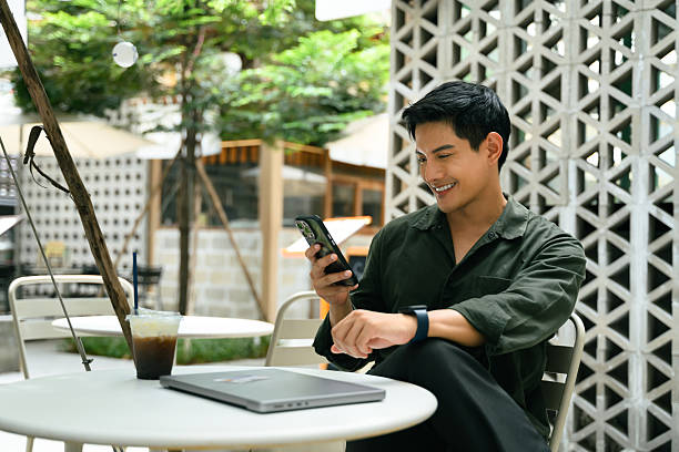 istock Smiling man relaxes at an outdoor cafe and using smartphone beside a closed laptop 2216213021