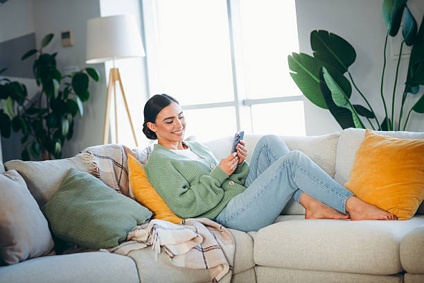 istock Young woman relaxing on a cozy couch at home while using her smartphone in a bright and beautifully decorated living room 2216213197