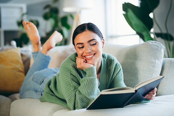 istock Young woman smiling while reading a book at home on a cozy sofa surrounded by natural light and greenery 2216213223