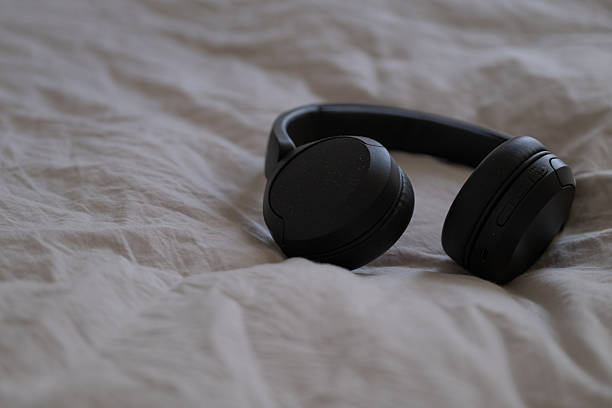 istock Black wireless headphones resting on soft wrinkled bedding. 2216216012
