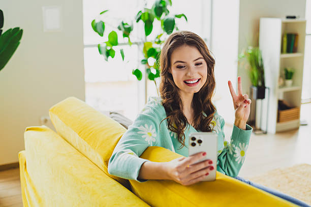 istock Charming woman taking a cheerful selfie at home while sitting on a cozy yellow sofa in a modern living room with natural daylight 2216218761