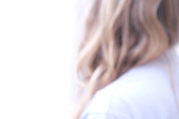 Close-up shot of a person with blonde hair seen from behind or three-quarter view. The image is softly focused, highlighting the texture of the hair and shoulder. The face is not visible, creating a sense of intimacy and anonymity.