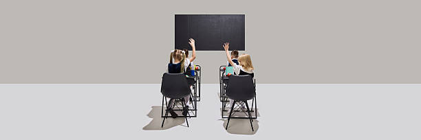 istock Curious children raising hands in front of chalkboard during classroom lesson, showing eagerness to answer questions. 2216224861