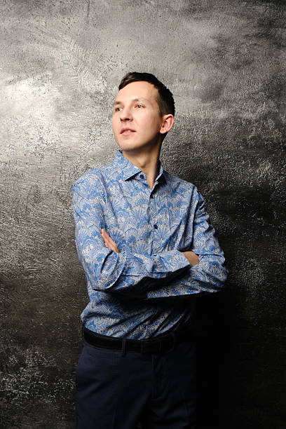 A trendy young man confidently showcases his unique style in a vibrant patterned shirt against a textured background