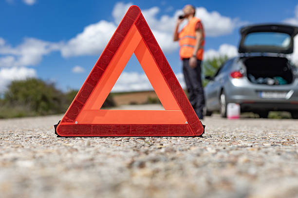 istock Warning triangle on the road with broken car and driver calling for help 2216229265
