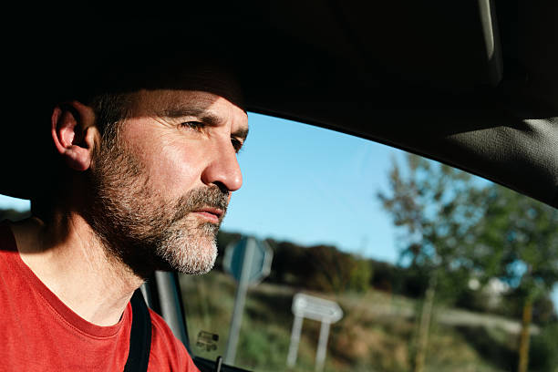 Segovia province. Spain. Mature man with a grey beard, wearing a vibrant red t-shirt, driving a car on a sunny day through the countryside