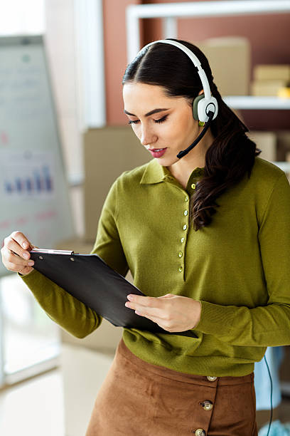 istock Young professional woman in stylish attire reviewing documents in an office setting, using a headset for communication 2216230297