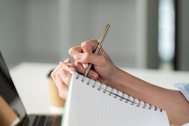 istock Writing and Focus. An individual jotting down notes in a notebook while working at a laptop. 2216230345