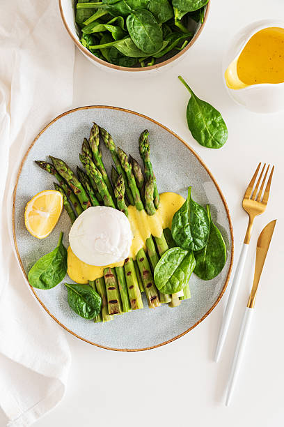 Poached egg with grilled asparagus, spinach, and hollandaise sauce on white table. Top view