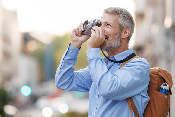 istock Mature man exploring a city with a camera and backpack on a sunny day 2216236629