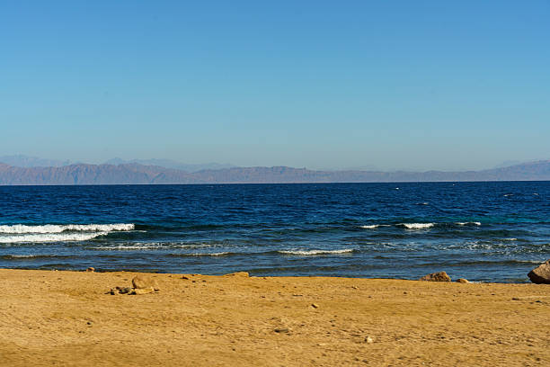 A beautiful blue ocean with a sandy beach in the background. The sky is clear and the sun is shining brightly