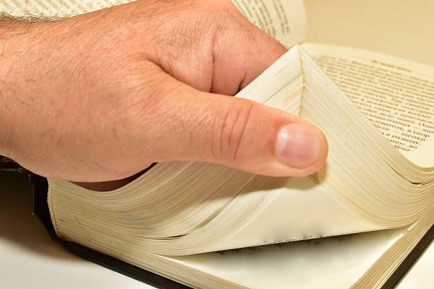 A man's hand turns the pages of a book lying on the table.