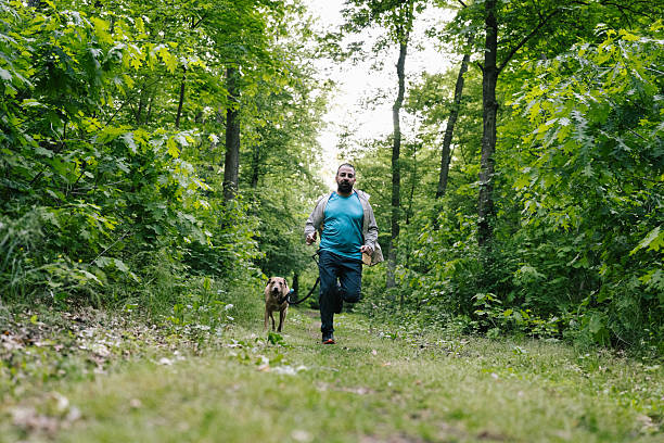 istock Canicross : a man runs with his mixed-breed dog through the forest 2216244150