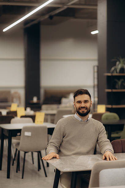 istock Man Smiling While Sitting at a Table in a Modern Furniture Store 2216246824