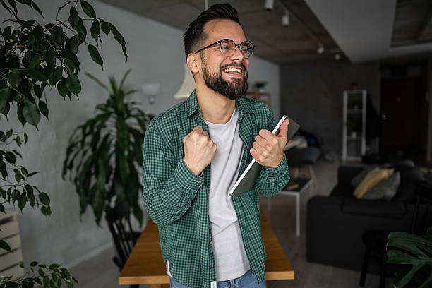 istock Excited young man celebrating success while holding tablet at home 2216251728