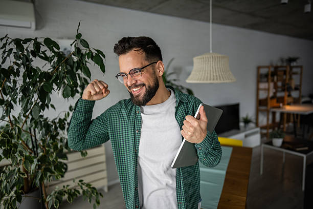 istock Enthusiastic young man celebrating success with tablet in hand at home 2216251767