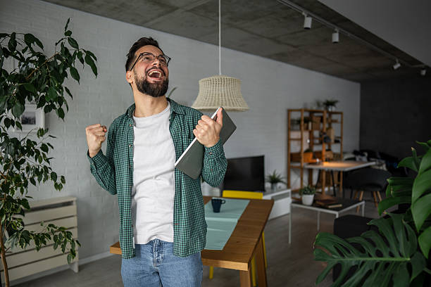 istock Young man celebrating success while holding digital tablet at home 2216251797