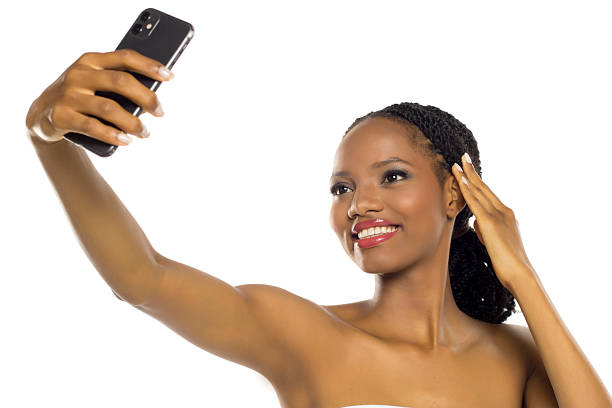 Smiling black woman with makeup taking a selfie, studio shot on white background.