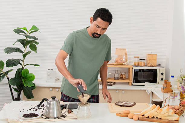 istock Middle-aged bearded Asian man grinds coffee beans with traditional coffee grinder using hand-crank to make the coffee beans powdered for drink in morning at home. Healthy lifestyle concept. 2216257345
