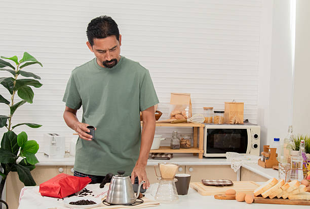 istock Middle-aged bearded Asian man grinds coffee beans with traditional coffee grinder using hand-crank to make the coffee beans powdered for drink in morning at home. Healthy lifestyle concept. 2216257348