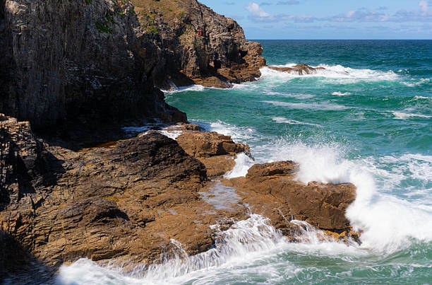 The sun shines down onto waves smashing into the rocky coastline around Perranporth Beach in Cornwall.