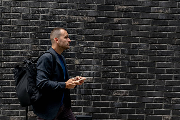 istock Businessman walking and using his smartphone in front of a black brick wall 2216267652