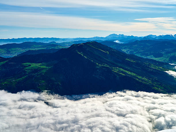 istock Mountain peak rises above clouds in bright daylight with distant hills and valleys in the background 2216268780