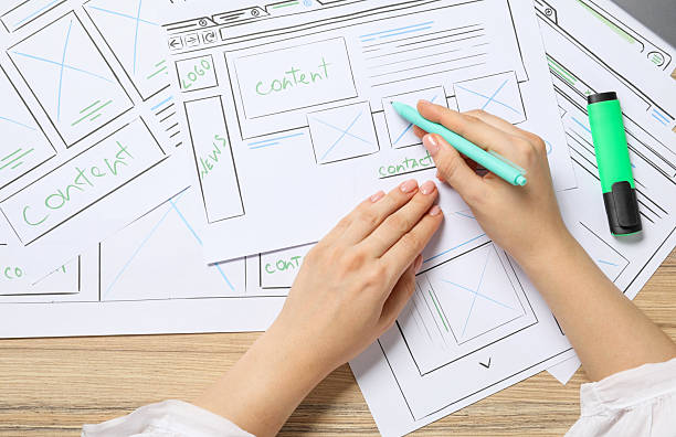istock Website designer creating wireframe on paper with pen at wooden table, top view 2216272627