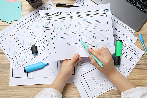 istock Website designer creating wireframe on paper with pen at wooden table, top view 2216272666