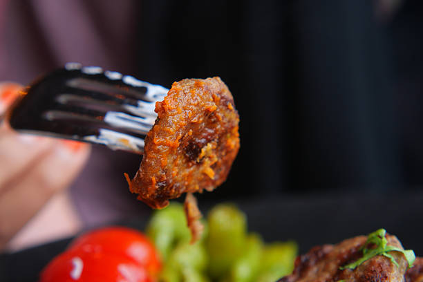 A person is lifting a meatball with a fork alongside colorful vegetables.