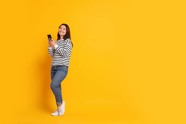 istock Smiling young woman with smartphone on yellow background. Space for text 2216274390