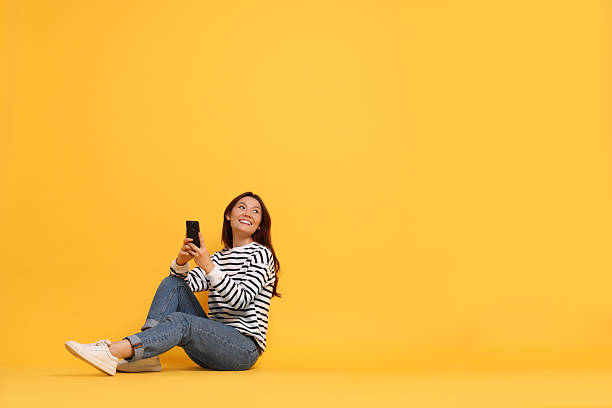 istock Smiling young woman with smartphone on yellow background. Space for text 2216274465