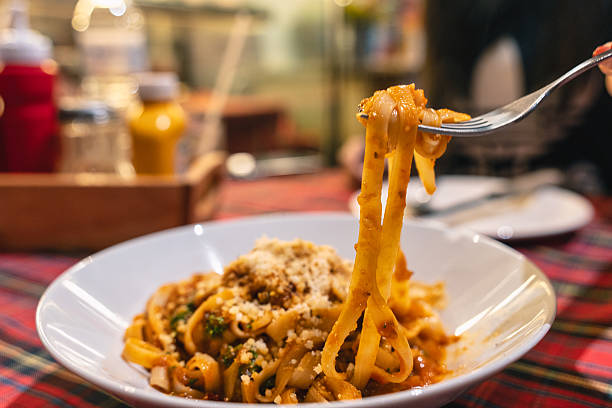 istock Fork lifting cooked Tagliatelle pasta served with savory meat sauce and cheese in white plate 2216274880