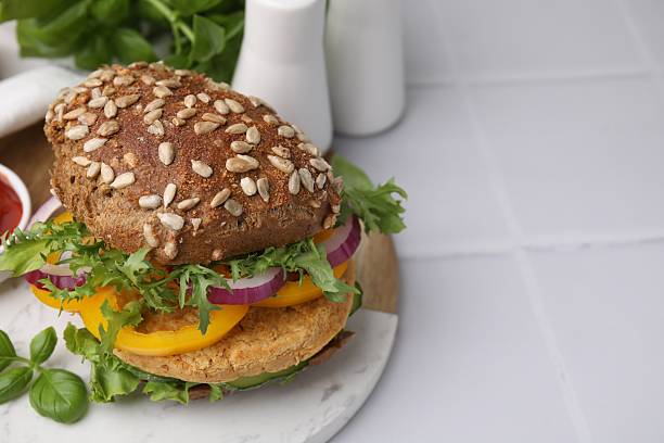 istock Delicious vegan burger with chickpea cutlet on white tiled table, closeup. Space for text 2216275236