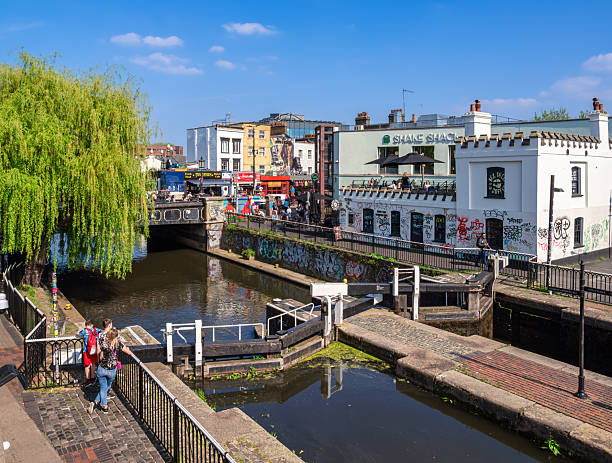 London, United Kingdom - April 28, 2025: A vibrant urban canal scene with a bridge, graffiti, and people walking.